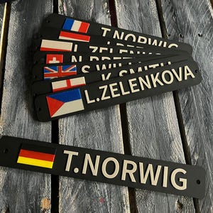 以下が含まれることがあります： 白文字と国旗が付いた黒いネームプレート。ネームプレートには、フランス、イギリス、チェコ共和国の名前と国旗が表示されています。1つのネームプレートには、ドイツの国旗とT. NORWIGという名前が表示されています。