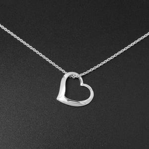 Puede incluir: Un collar plateado con un colgante en forma de corazón. El colgante es un diseño de corazón abierto y sólido, suspendido de una fina cadena. El collar se muestra sobre un fondo oscuro.