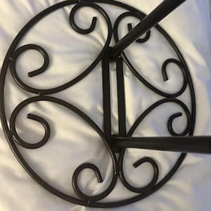 May include: Black metal plant stand with a circular top featuring decorative scrollwork. The stand has three legs and is designed to hold a potted plant. The scrolled design adds a touch of elegance to the plant stand.