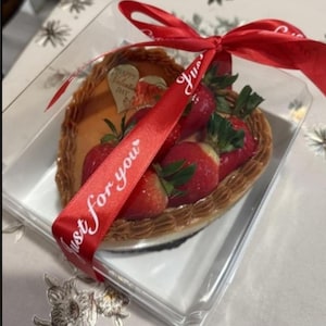 May include: A heart-shaped dessert with fresh strawberries, presented in a clear plastic container. The dessert is decorated with a red ribbon that says "Just for you". A small gold heart with "Happy Valentine's Day" is also visible.