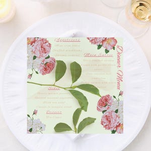 May include: A dinner menu with floral accents, featuring pink roses and green leaves, rests on a white plate. The menu includes sections for appetizers, main course, and dessert. A fork and knife are placed on either side of the plate, with candles and flowers in the background.