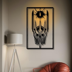 May include: Black metal wall art featuring a stylized design of a crown and an eye, set within a rectangular frame. The artwork is illuminated from behind, creating a glowing effect. The design is reminiscent of fantasy themes.
