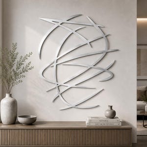 Pode incluir: Uma grande escultura de parede em metal de cor prateada, apresentando uma série de linhas curvas que se cruzam formando uma forma circular abstrata. A peça é composta por tiras de metal lisas e planas num padrão sobreposto.