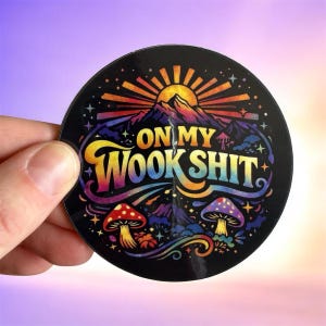 May include: A round black sticker with the text "ON MY WOOK SHIT" in colorful, stylized lettering. The design includes a mountain range, a setting sun, mushrooms, and a rainbow, all in vibrant colors.
