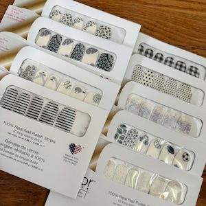 May include: A collection of nail polish strips in various designs, including animal print, paisley, sports balls, and stripes. Each package contains 16 long-lasting strips. The packaging features the text "100% Real Nail Polish Strips."