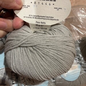 May include: A skein of light gray yarn with a label that reads "60% Cotone/Baumwolle/Coton/Cotton 40% Acrilico HB Microfibra/Polyacryl/Acrylique/Acrylic Peso Netto 50 g e = 115 m/125,3 yds"