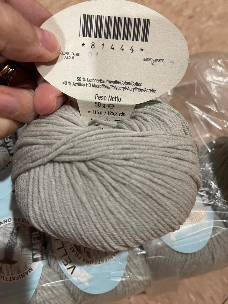 May include: A skein of light gray yarn with a label that reads "60% Cotone/Baumwolle/Coton/Cotton 40% Acrilico HB Microfibra/Polyacryl/Acrylique/Acrylic Peso Netto 50 g e = 115 m/125,3 yds"