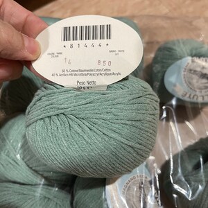 May include: A skein of light green yarn with a label that reads "60% Cotone/Baumwolle/Coton/Cotton 40% Acrilico HB Microfibra/Polyacryl/Acrylique/Acrylic Peso Netto 50 g e * 8 1 4 4 4 * 14 850"