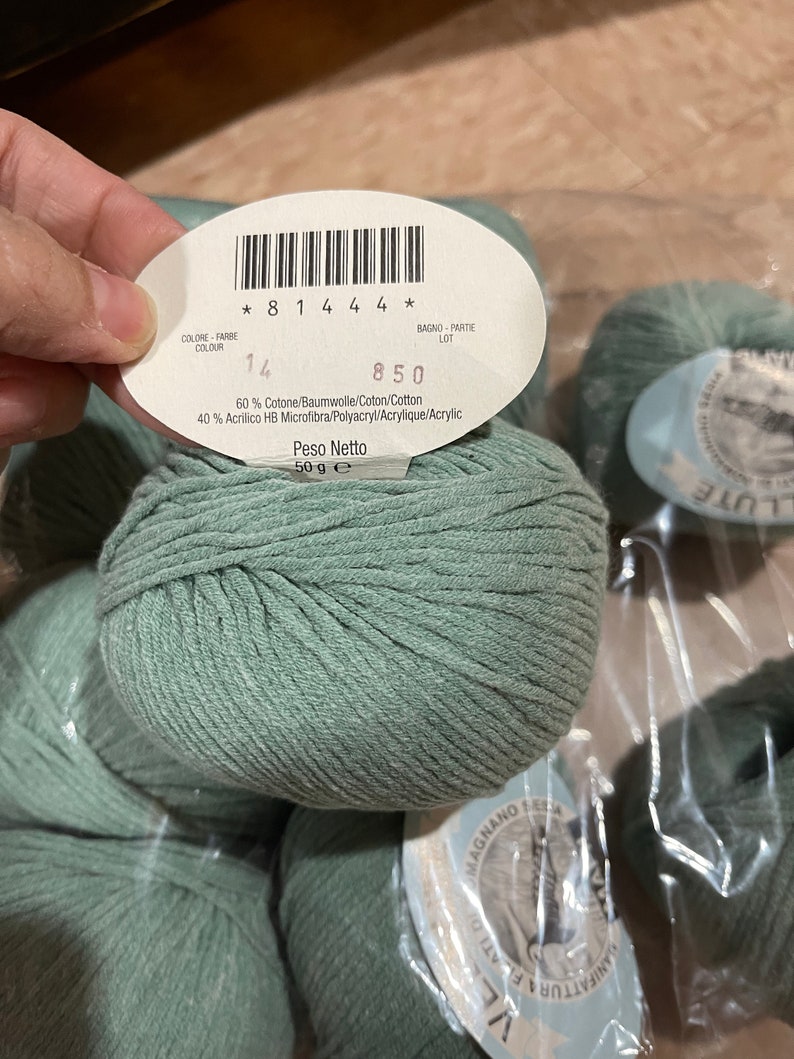 May include: A skein of light green yarn with a label that reads "60% Cotone/Baumwolle/Coton/Cotton 40% Acrilico HB Microfibra/Polyacryl/Acrylique/Acrylic Peso Netto 50 g e * 8 1 4 4 4 * 14 850"