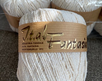 May include: A close-up of a white yarn ball with a brown label that reads "Ital Fantasia Industria Tessile Alta Fantasia Monte Murlo (FI)"