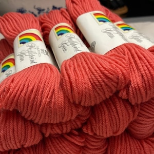 May include: A stack of coral-colored yarn skeins with rainbow labels that read "Middlepoint Yarn" and "100% Wool".