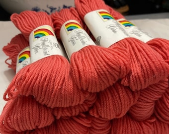 May include: A stack of coral-colored yarn skeins with rainbow labels that read "Middlepoint Yarn" and "100% Wool".