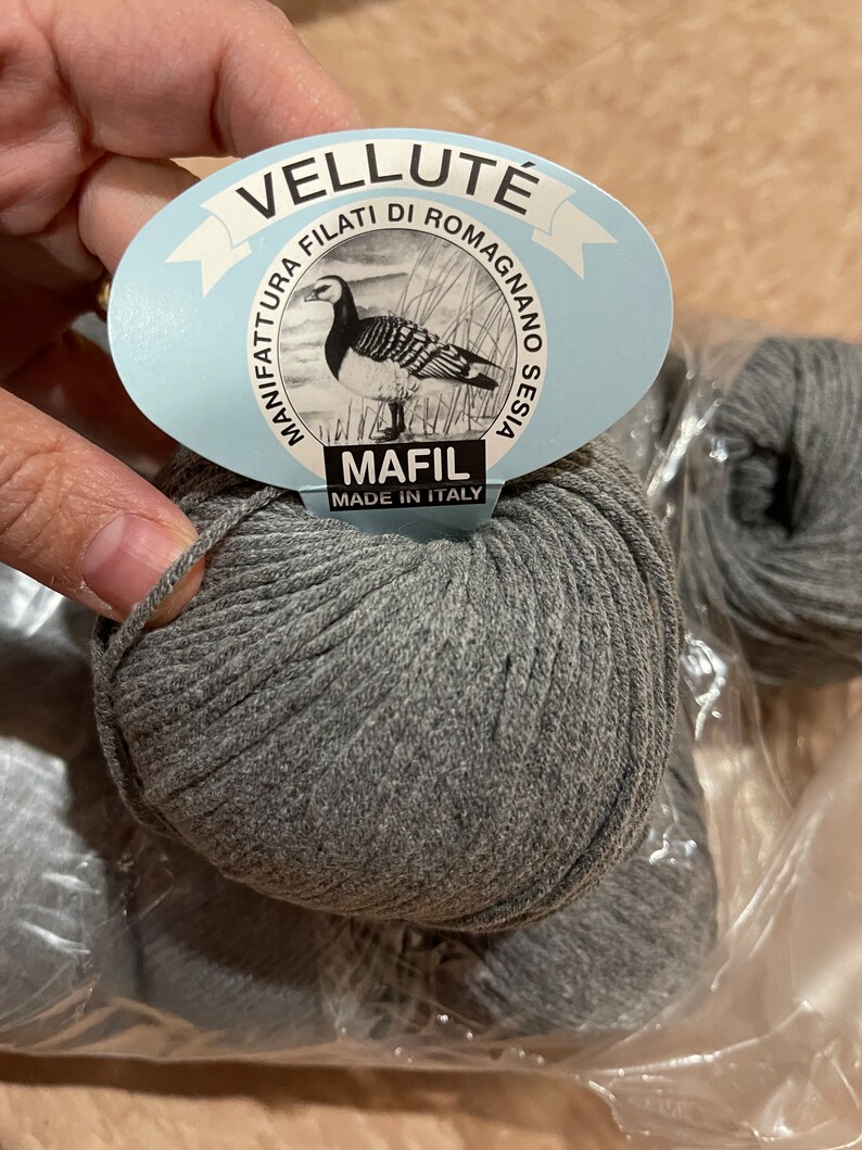 Op de afbeelding: Drie bollen grijs garen in een plastic zak. Het garen is gelabeld met "Vellut&eacute;" en "Mafil Made in Italy".
