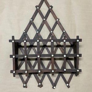 May include: A dark brown wooden wall shelf with a diamond pattern and a triangular top. The shelf has two horizontal shelves and is held together with small white pegs. The shelf is designed to be mounted on a wall.