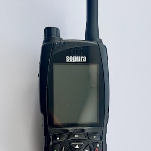 Puede incluir: Radio Sepura negra con pantalla y teclado. La radio tiene una antena negra con "TSG" impreso. El teclado tiene n&uacute;meros y s&iacute;mbolos. La radio est&aacute; dise&ntilde;ada para la comunicaci&oacute;n.