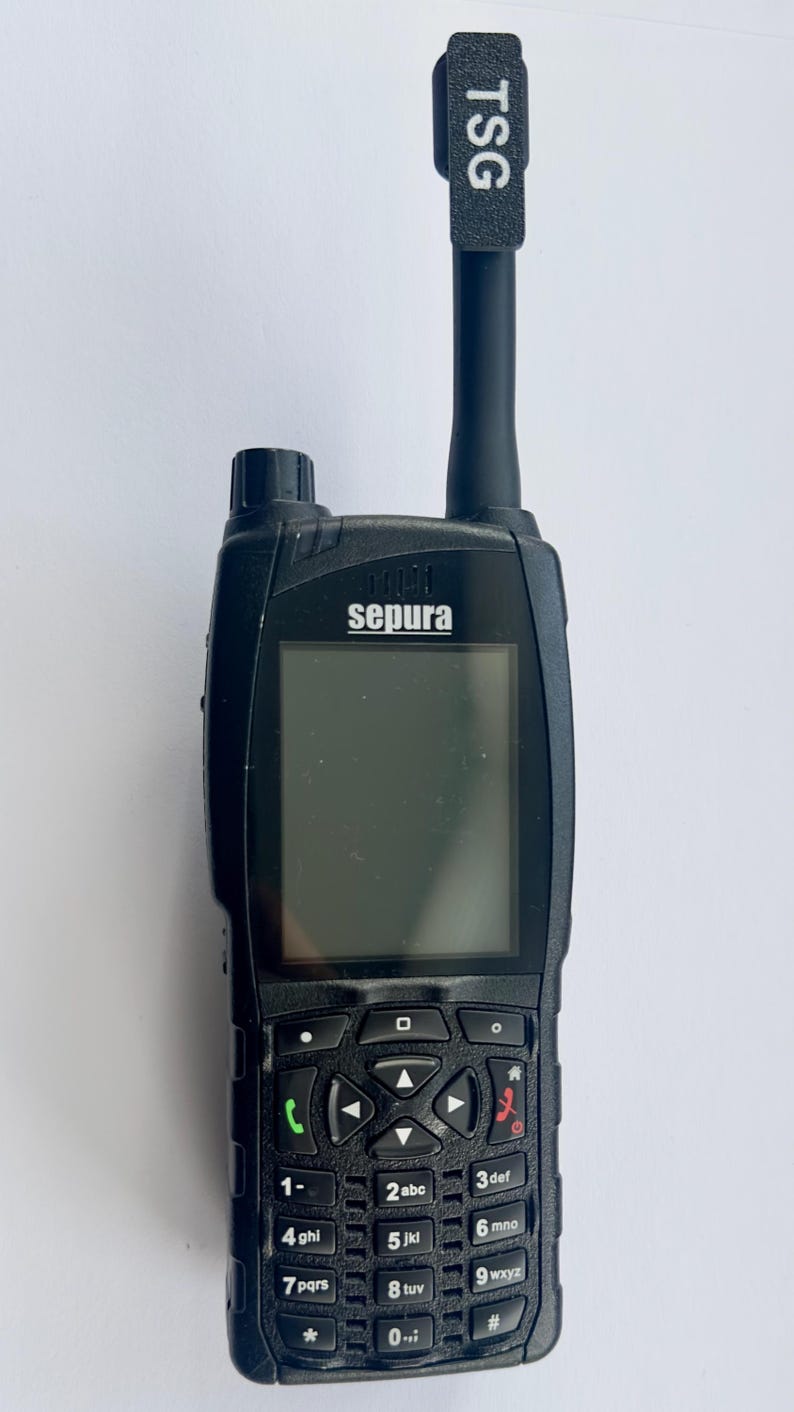 Puede incluir: Radio Sepura negra con pantalla y teclado. La radio tiene una antena negra con "TSG" impreso. El teclado tiene n&uacute;meros y s&iacute;mbolos. La radio est&aacute; dise&ntilde;ada para la comunicaci&oacute;n.