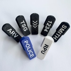 Puede incluir: Colecci&oacute;n de accesorios rectangulares negros y de colores con varios textos y s&iacute;mbolos blancos. El texto incluye "ARV", "TSG", "1234", "SMITH", "POLICE" y "RPU". Los accesorios tienen una superficie texturizada.