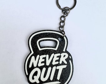 Puede incluir: Un llavero negro con forma de pesa rusa, superficie texturizada y el texto impreso en blanco NEVER QUIT. El llavero cuenta con una argolla de metal oscuro sujeta por una cadena corta, funcionando como un accesorio práctico para las llaves.