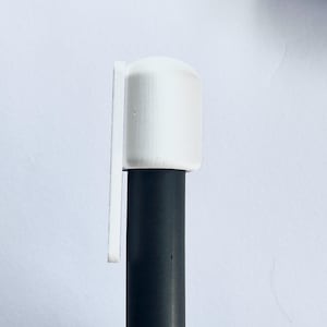 Puede incluir: Una tapa cil&iacute;ndrica blanca con una leng&uuml;eta rectangular adjunta, colocada sobre un objeto cil&iacute;ndrico negro. La tapa tiene una superficie texturizada. El fondo es de color blanquecino.