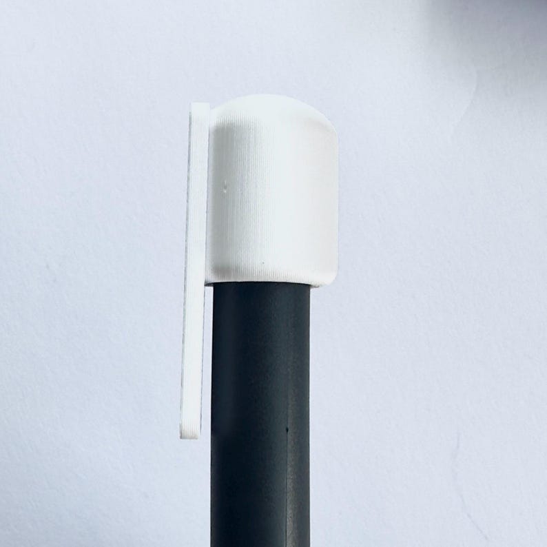 Puede incluir: Una tapa cil&iacute;ndrica blanca con una leng&uuml;eta rectangular adjunta, colocada sobre un objeto cil&iacute;ndrico negro. La tapa tiene una superficie texturizada. El fondo es de color blanquecino.