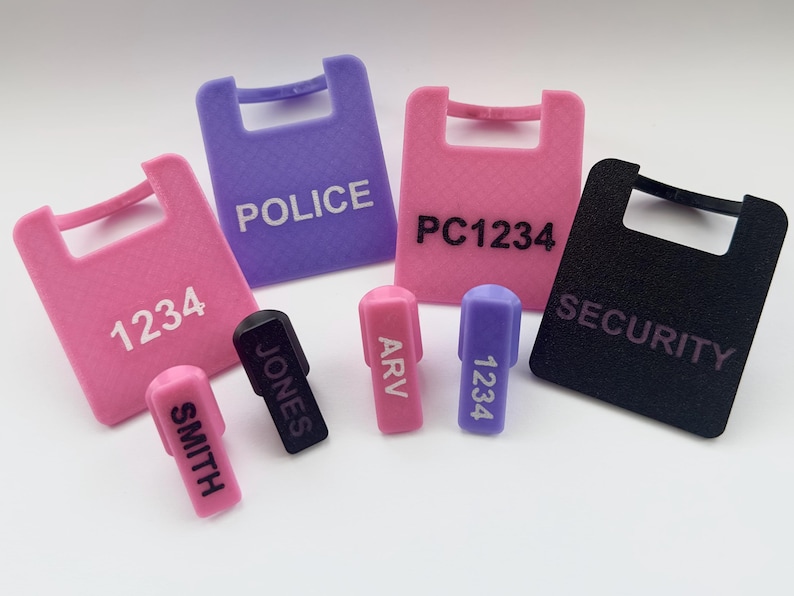 Puede incluir: Una colecci&oacute;n de etiquetas de seguridad y llaveros de colores. Las etiquetas son rosas, moradas y negras, con las palabras "POLICE", "SECURITY" y n&uacute;meros impresos. Los llaveros son rosas, morados y negros, con nombres y n&uacute;meros.