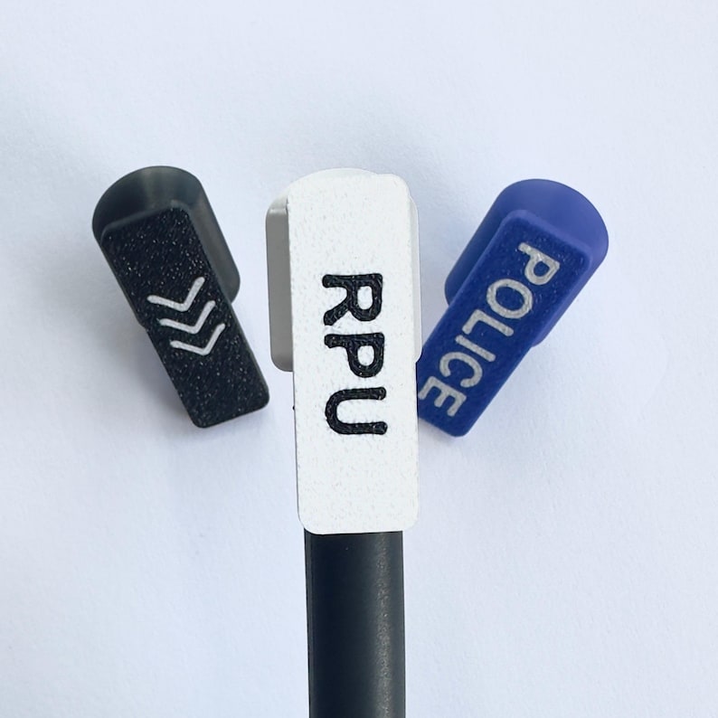 Puede incluir: Tres tapas de bol&iacute;grafo en negro, blanco y azul. La tapa negra tiene flechas blancas, la tapa blanca tiene las letras "RPU" y la tapa azul dice "POLICE" en blanco. Sobre un fondo blanco.