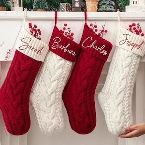 May include: Four cable-knit Christmas stockings, red and white, hang from a white mantel. Each stocking is personalized with a name embroidered in cursive: Sarah, Barbara, Charles, and Joseph. The stockings are approximately 13 inches (33 cm) long.