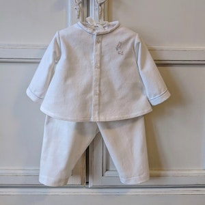 May include: White baby pyjamas with a long-sleeved button-up top and matching trousers. The top has a small embroidered bunny on the front.