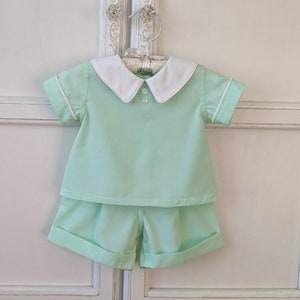 May include: A light green two-piece outfit for a baby or toddler. The outfit includes a short-sleeved shirt with a white collar and a pair of shorts.