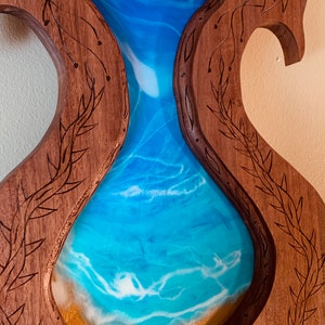 May include: A wooden wall art piece with a carved frame and a resin inlay of blue and white waves. The frame is carved with a floral design.