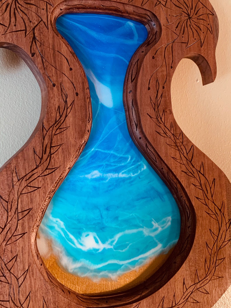 May include: A wooden wall art piece with a carved frame and a resin inlay of blue and white waves. The frame is carved with a floral design.