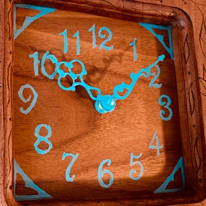 May include: A wooden clock face with blue painted Roman numerals and hands. The clock face is set in a wooden frame with carved details.