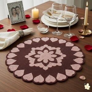 May include: A brown and pink heart-shaped placemat on a wooden table, with a floral design in the centre and heart shapes around the edge. The table is set for a romantic dinner, with wine glasses, plates, and candles.