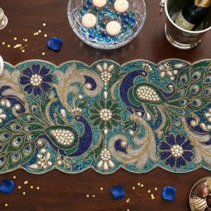 Può includere: Runner da tavolo con pavoni in perline nei toni del verde acqua, blu e oro. Il runner presenta un bordo smerlato e intricati disegni floreali e di pavoni. La tavola è apparecchiata con candele, fiori e bicchieri.