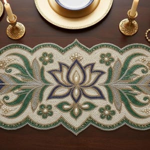 Może przedstawiać: Beaded bieżnik na stół z kwiatowym i liściastym wzorem w odcieniach zieleni, niebieskiego i złota. Bieżnik jest kremowy z falistą krawędzią. Nakrycie stołu obejmuje świece, talerze i miskę winogron.