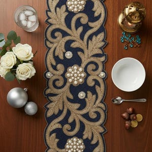 May include: A navy blue and gold beaded table runner with floral and scrollwork designs. The runner features pearl-like embellishments and is displayed on a wooden table. Other items include a glass of water, flowers, and decorative items.