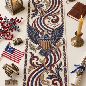 May include: A patriotic table runner with a central design featuring a blue eagle, red and blue stripes, and gold embellishments. The runner is surrounded by decorative elements like a miniature American flag, a candle, and a compass.