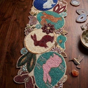 Puede incluir: Camino de mesa de Pascua con cuentas con cuatro diseños ovalados con siluetas de conejos en blanco, naranja, burdeos y rosa. El corredor tiene un fondo turquesa, azul y crema con detalles florales y de hojas. Aproximadamente 91 cm de largo.