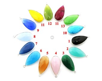 May include: A set of 13 teardrop-shaped gemstone pendants with silver bail settings. The pendants are arranged in a circle, with each pendant numbered from 1 to 13. The pendants are in various colors, including blue, green, pink, yellow, red, black, and turquoise.