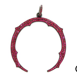 May include: A silver pendant with a crescent moon shape, encrusted with pink gemstones. The pendant has a delicate, intricate design.