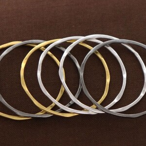 Peut inclure: Cinq bracelets en métal martelé, deux dorés et trois argentés, empilés sur un fond en tissu brun.