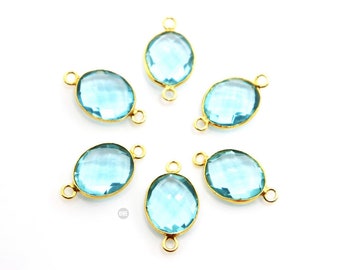 Op de afbeelding: Zes ovale turquoise blauwe edelsteen kralen met gouden metalen connector lussen. De kralen zijn gefacetteerd en hebben een heldere, glazige uitstraling.