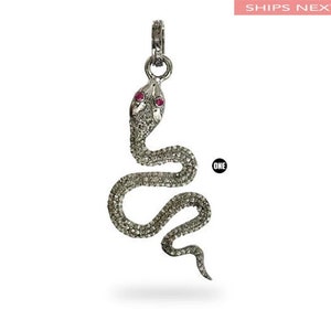 Könnte beinhalten: Ein silberner Schlangenanhänger mit einem mit Diamanten besetzten Körper und rubinroten Augen. Die Schlange ist in einer klassischen S-Form gewickelt.