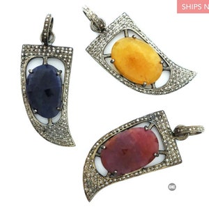 May include: Three silver pendants with a prong setting, each featuring a different colored gemstone. The pendants are shaped like a curved horn with a diamond-encrusted border. The gemstones are a blue sapphire, a yellow citrine, and a red ruby.