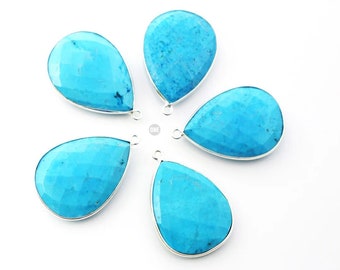 Op de afbeelding: Vijf druppelvormige turquoise hangers met zilverkleurige randen. Elke hanger heeft een facetgeslepen oppervlak en een kleine lus aan de bovenkant om aan een ketting of ander sieradenonderdeel te bevestigen. De hangers zijn op een witte achtergrond geplaatst.