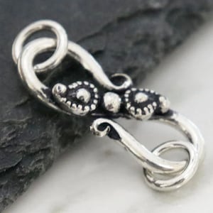 May include: Silver clasp with a decorative design featuring three round accents. The clasp is designed to be used for jewellery making.