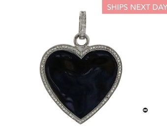 Puede incluir: Un colgante de plata en forma de corazón con un centro de esmalte negro y un halo de diamantes.