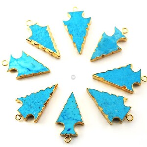 May include: Eight turquoise arrowhead pendants with gold-plated edges. The arrowheads are arranged in a circle on a white background.