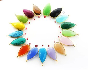 May include: A collection of teardrop-shaped gemstone pendants in various colors, including green, blue, pink, and orange. Each pendant has a gold-colored bezel and a small loop at the top for attaching to a chain or other jewelry component.