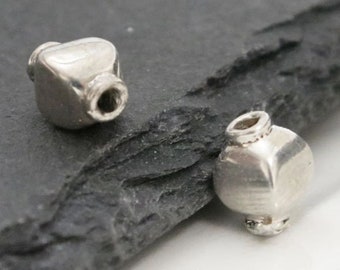 May include: Two silver metal beads with a rounded, slightly squared shape. The beads have a hole through the center for stringing.